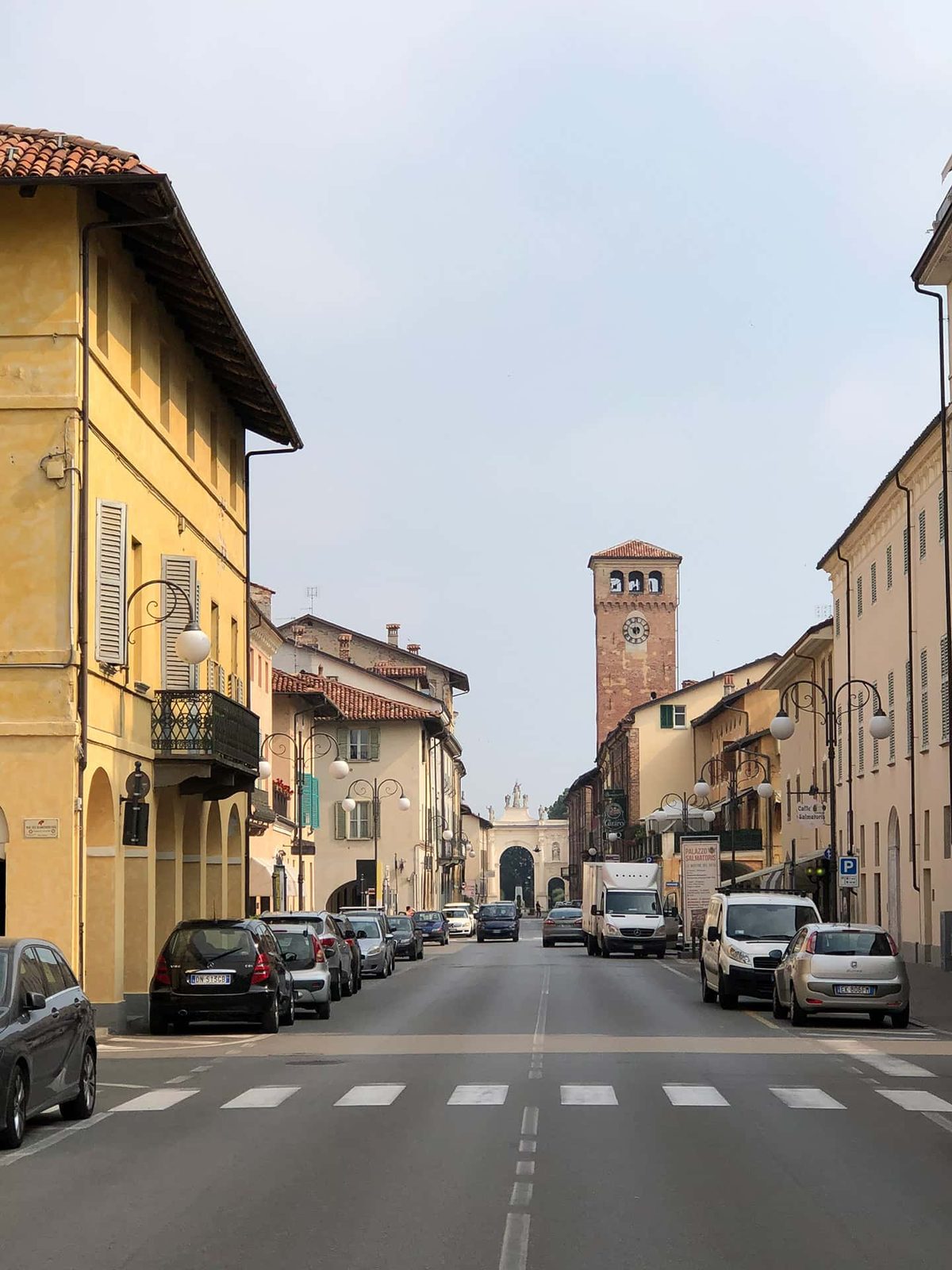 A quiet street in downtown Cherasco lined with yellow and ochre buildings, the clock tower in the distance