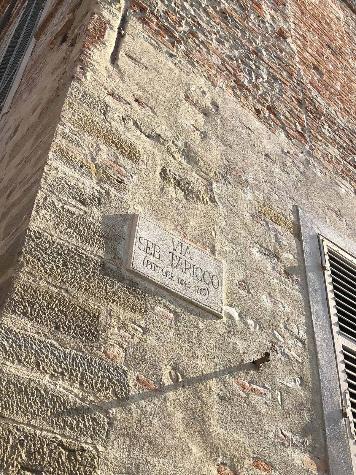 A stone street sign reading Via Seb. Taricco, Pittore, 1645 to 1710, on an old wall