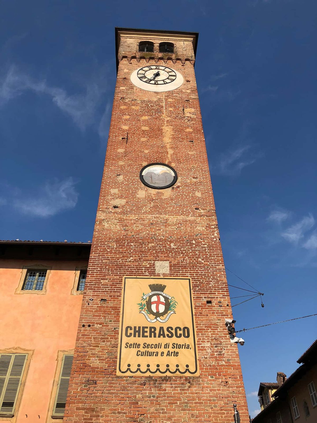 The brick clock tower in Cherasco, Italy, under a deep blue sky